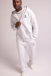 Person wearing a grey tracksuit with brand logos on a light gray background