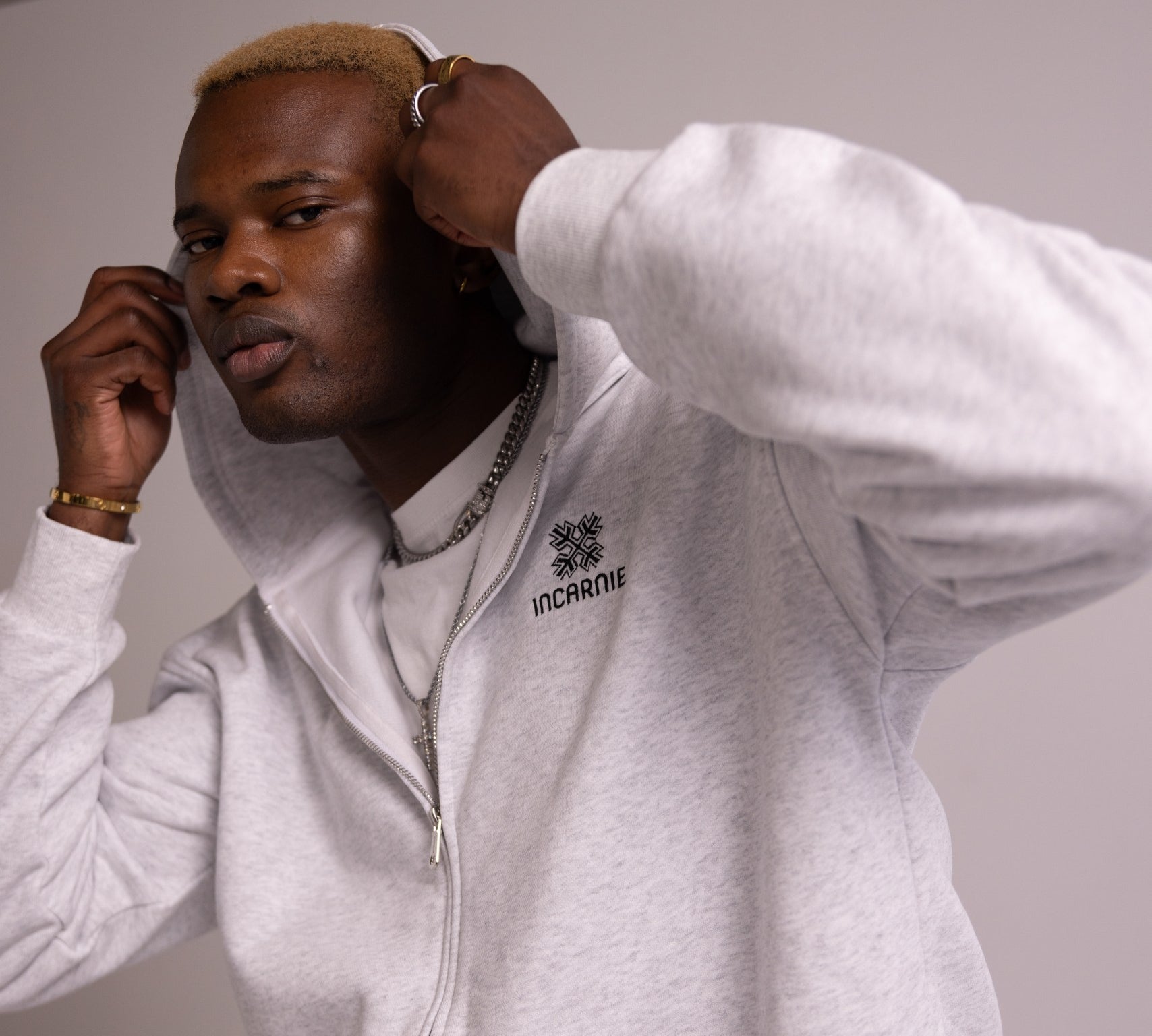 Person wearing a grey hoodie with a logo on a plain background