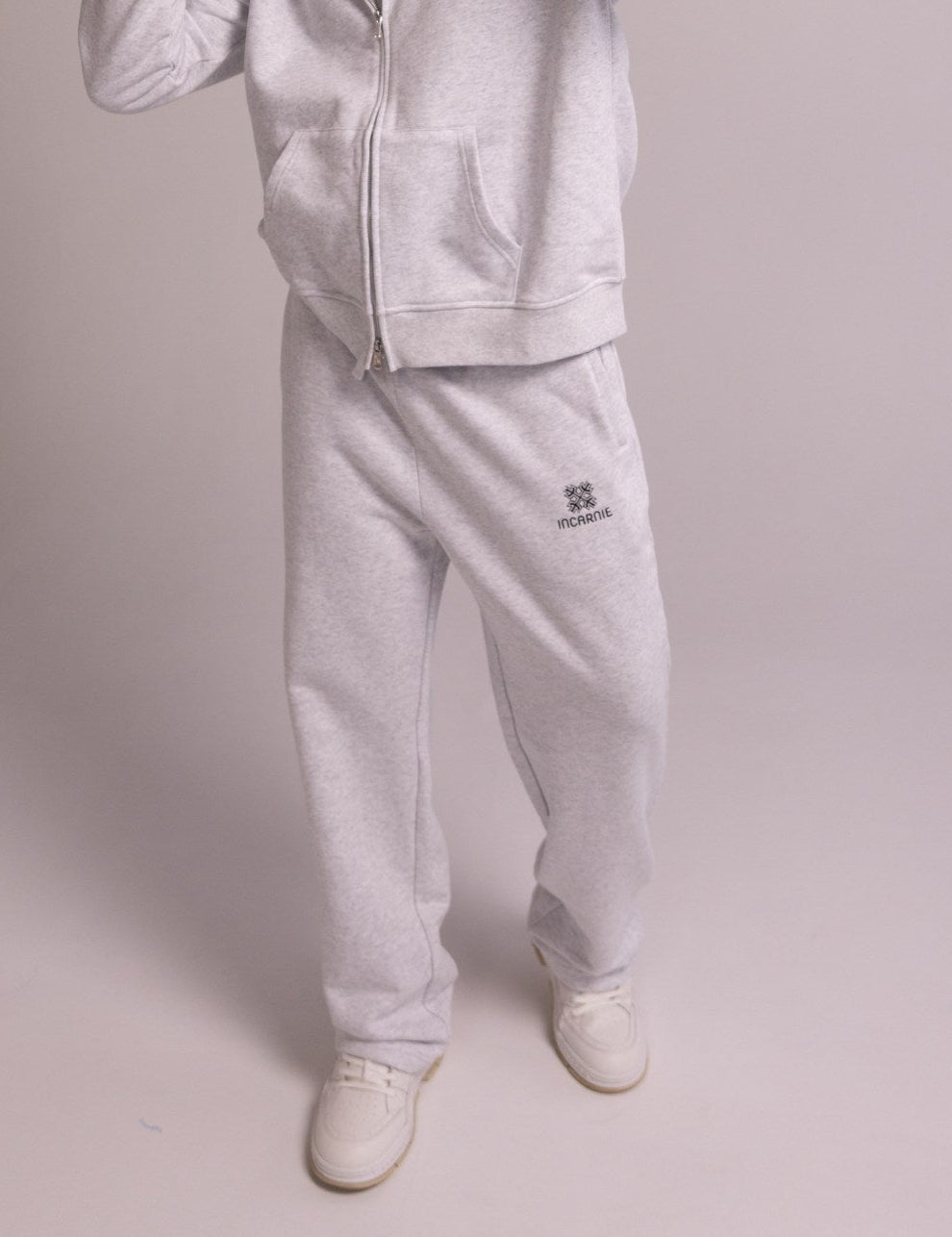 Person wearing a grey tracksuit with a brand logo on a plain background