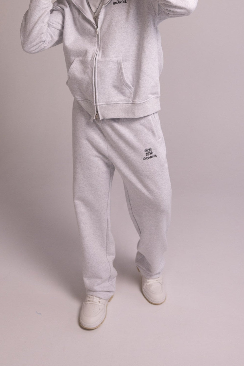 Person wearing a grey tracksuit with a brand logo on a plain background