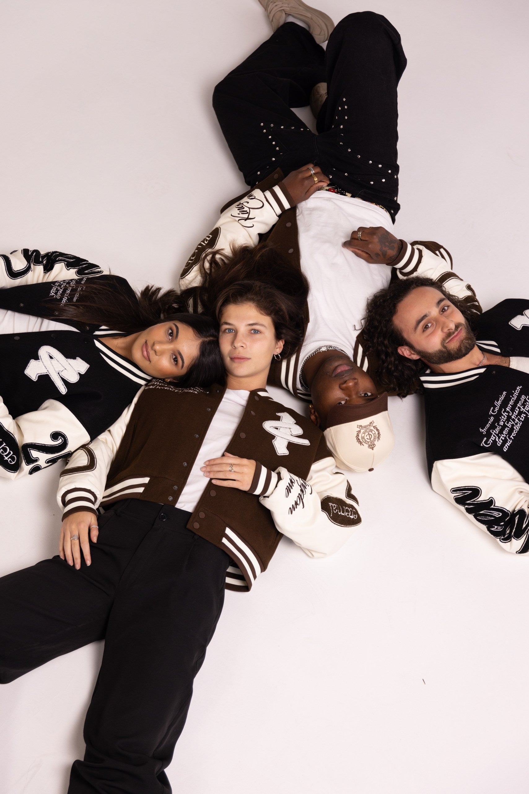 Five people wearing matching varsity jackets lying on a white background
