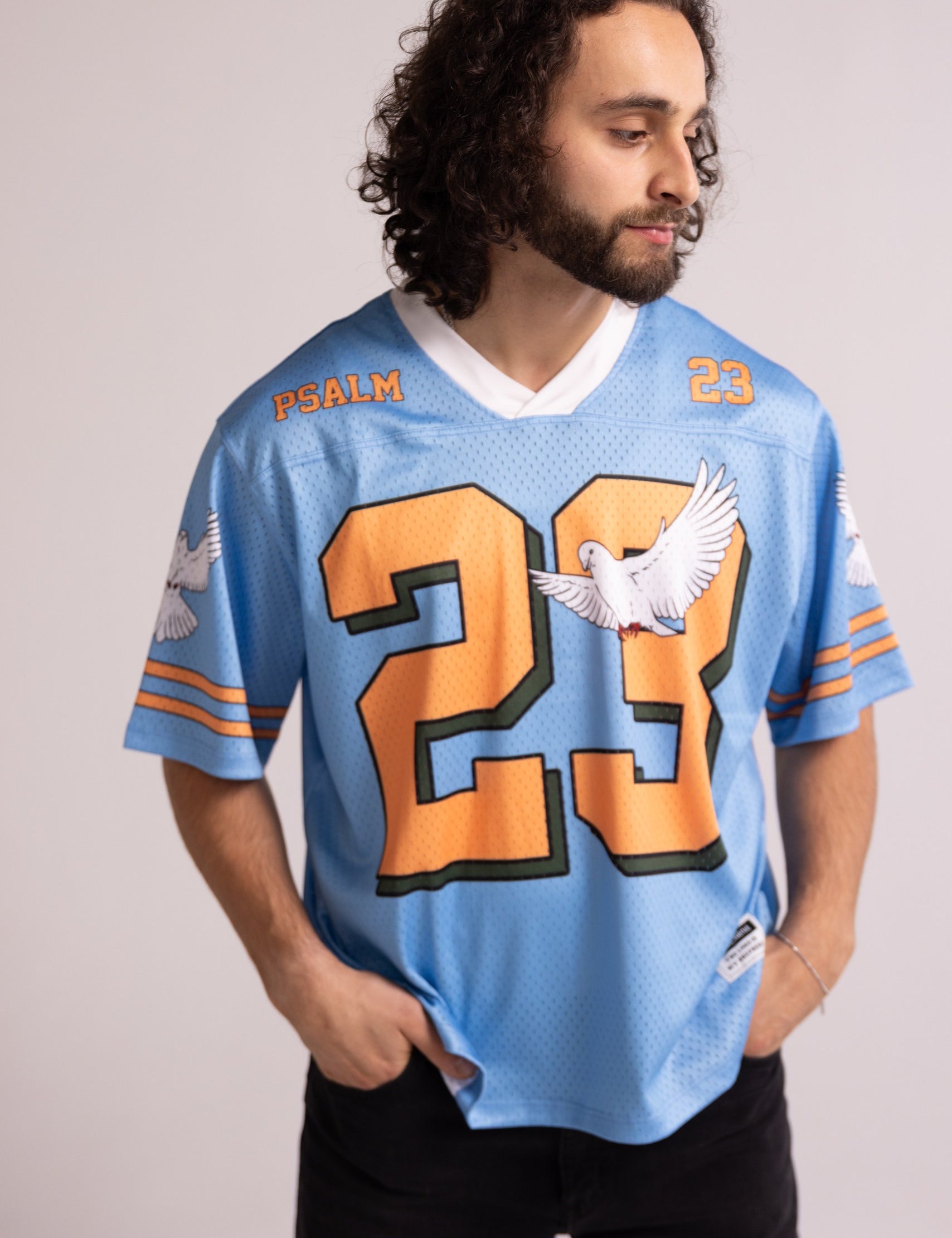 Man wearing a light blue sports jersey with orange numbers and text on a plain background