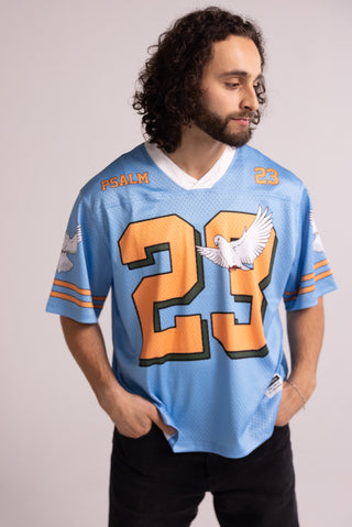 Man wearing a light blue sports jersey with orange numbers and text on a plain background