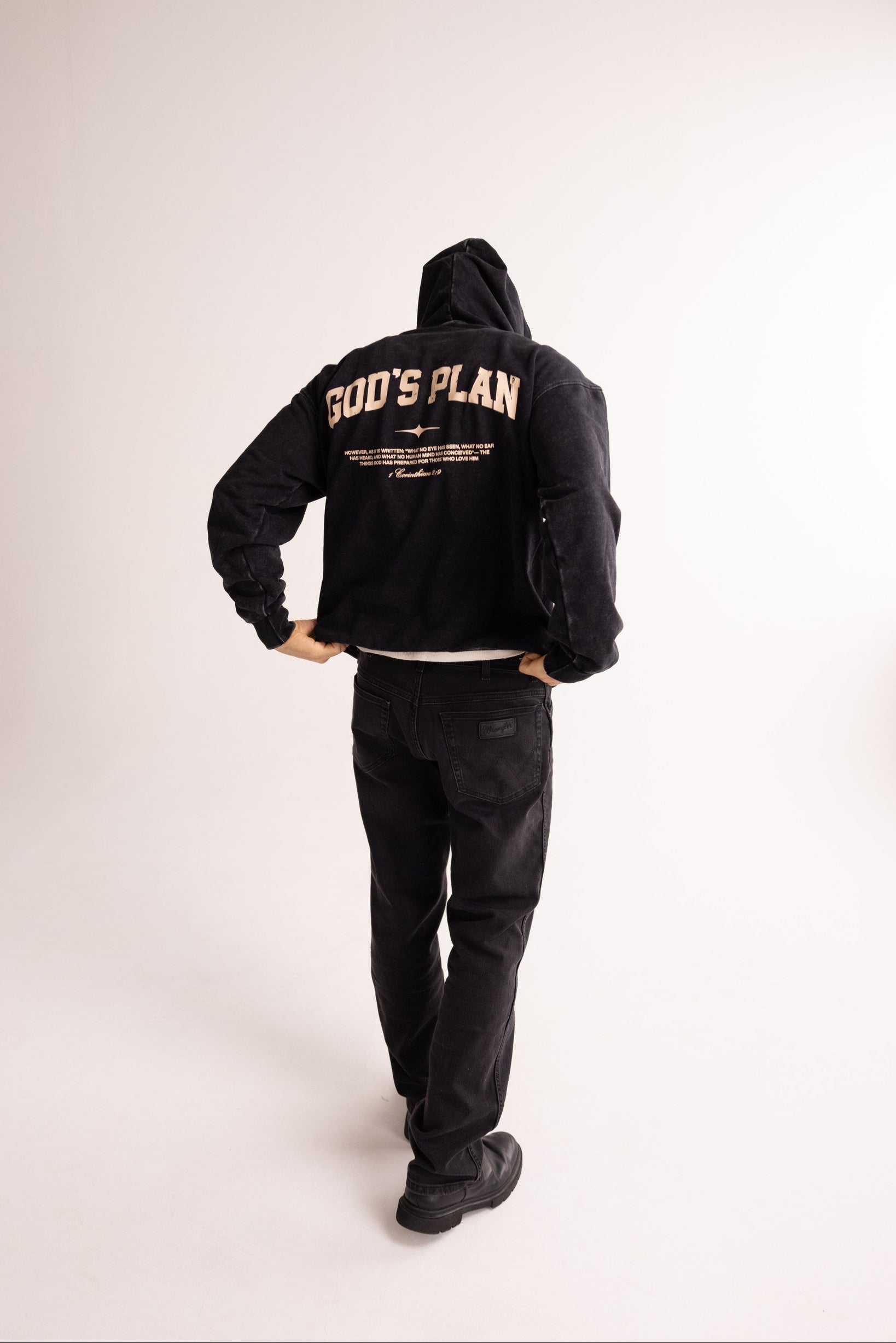 Person wearing a black hoodie with 'GOD'S PLAN' text on the back against a white background
