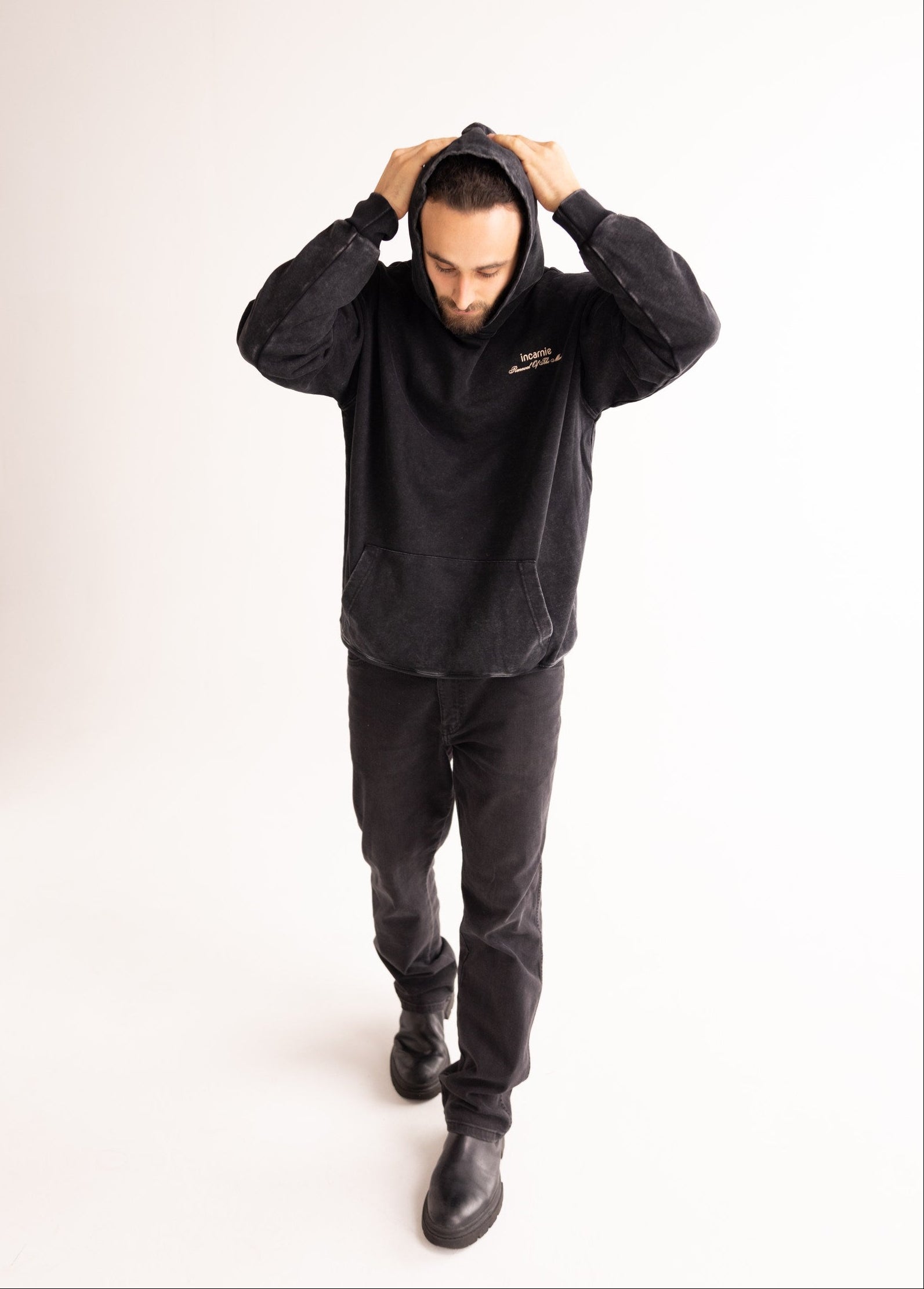 Person wearing a black hoodie and pants in a studio setting