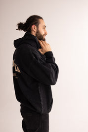 Man wearing a black hoodie with text on the back against a plain background