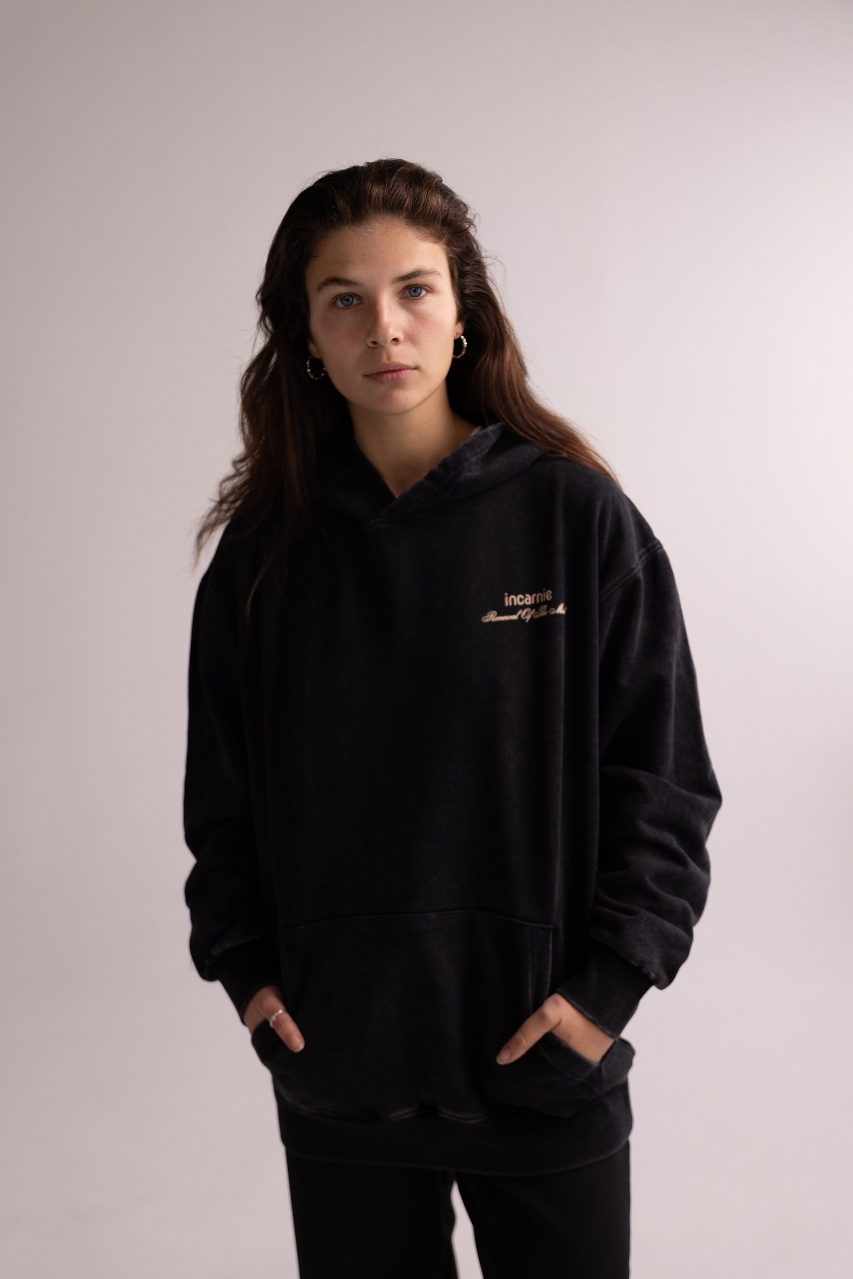 Person wearing a black hoodie with a logo on a plain background