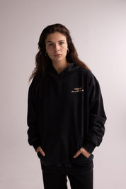 Person wearing a black hoodie with a logo on a plain background