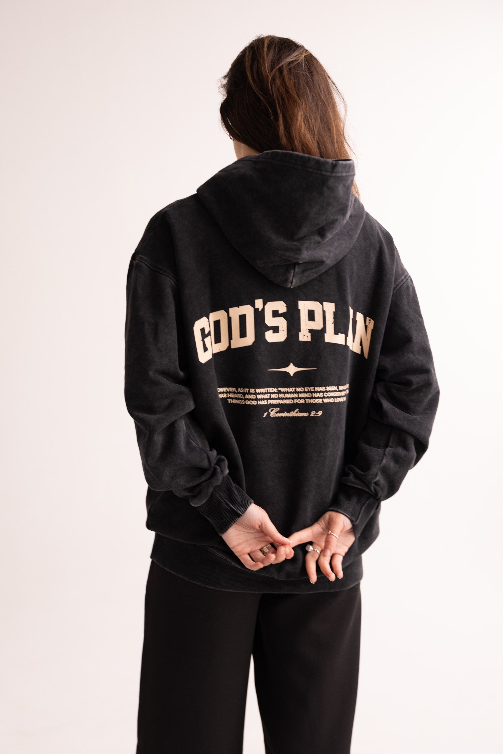 Person wearing a black hoodie with 'GOD'S PLAN' text on the back against a white background
