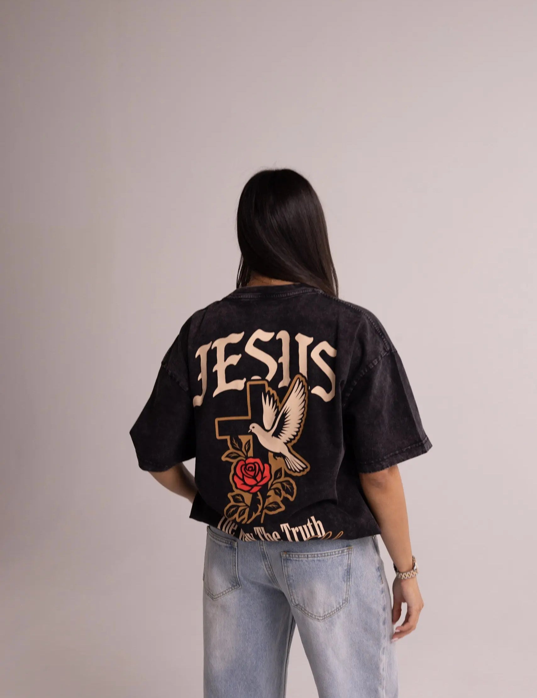 Person wearing a black t-shirt with 'Jesus' and dove design on the back, standing against a plain background.