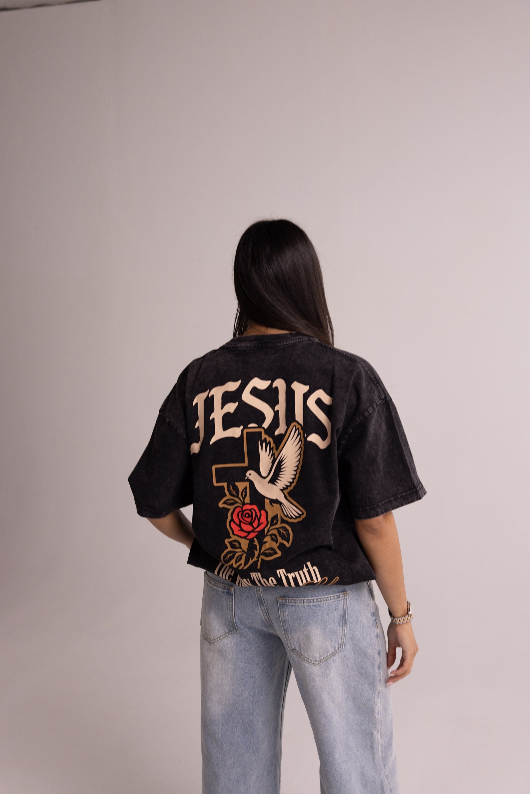 Person wearing a black t-shirt with 'Jesus' and dove design on the back, standing against a plain background.