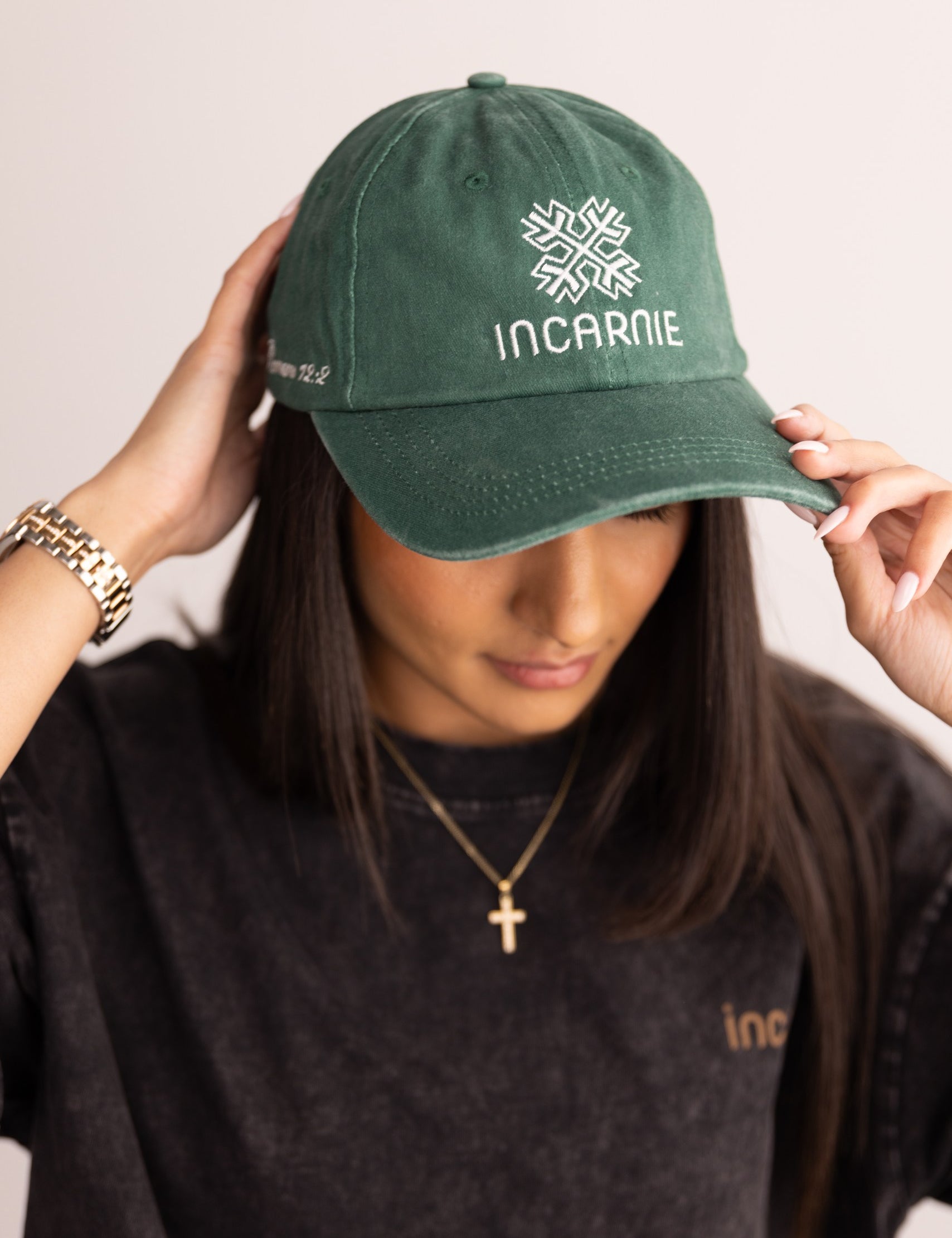 Person wearing a green cap with 'INCARNIE' logo and text, holding it above their head.