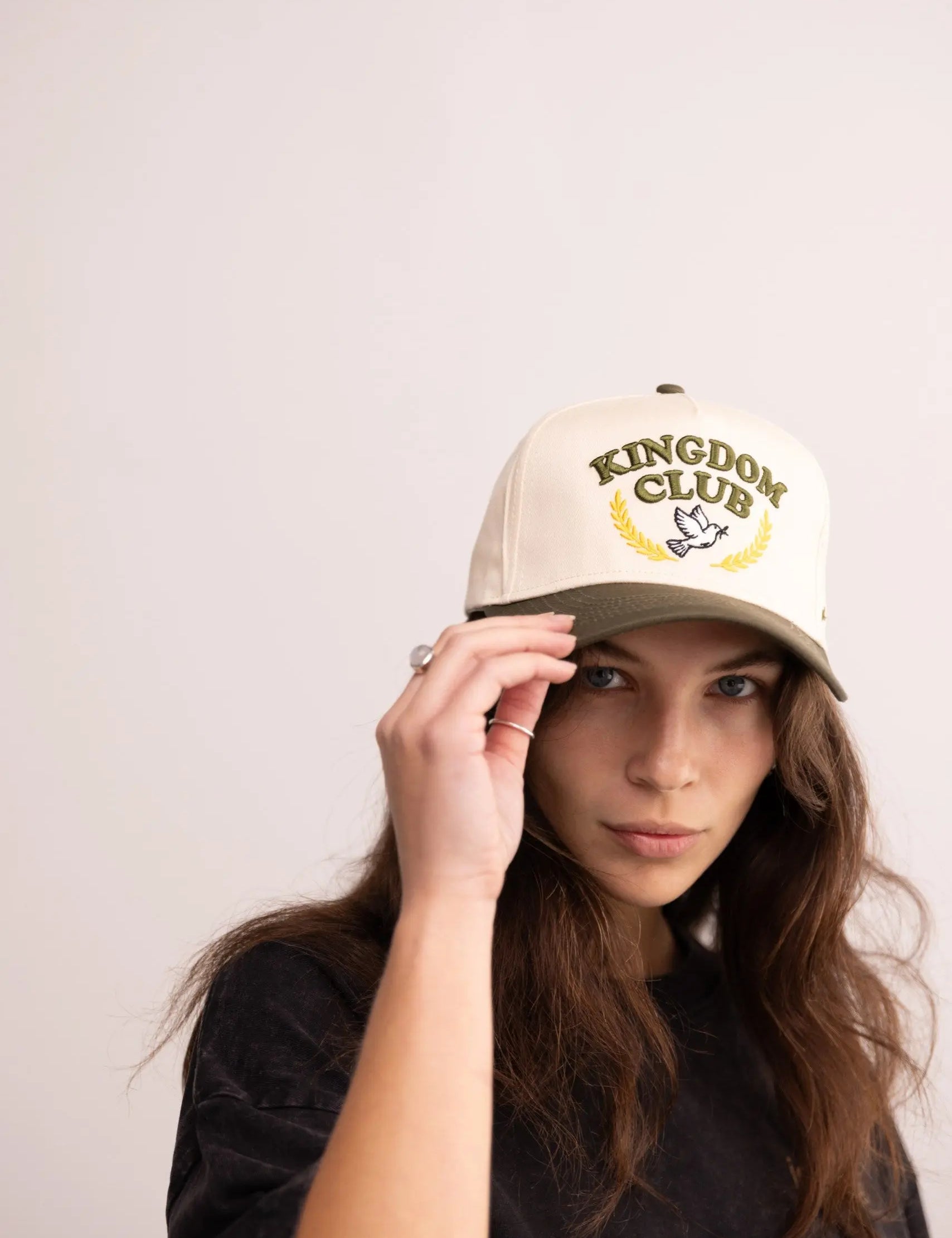 Person wearing a beige cap with 'Kingdom Club' logo on a plain background