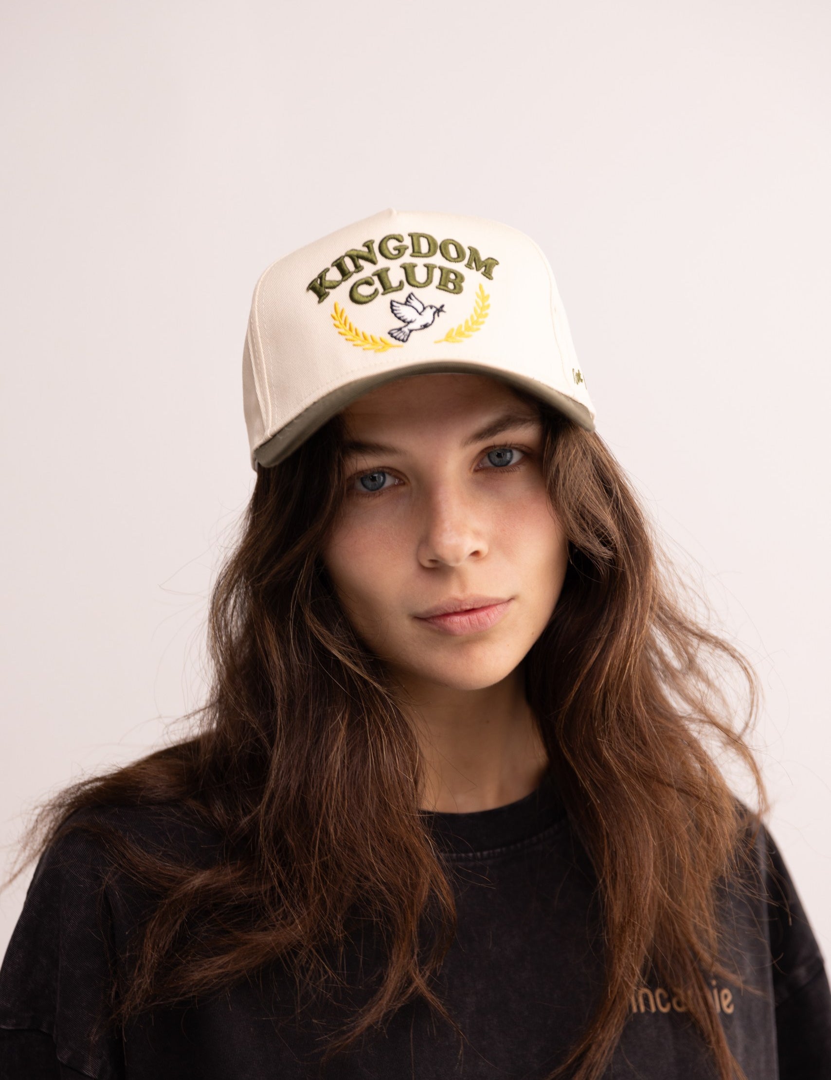 Person wearing a 'Kingdom Club' cap on a plain background