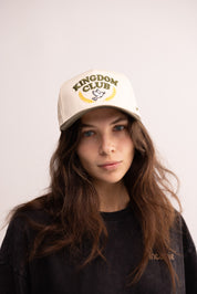Person wearing a 'Kingdom Club' cap on a plain background