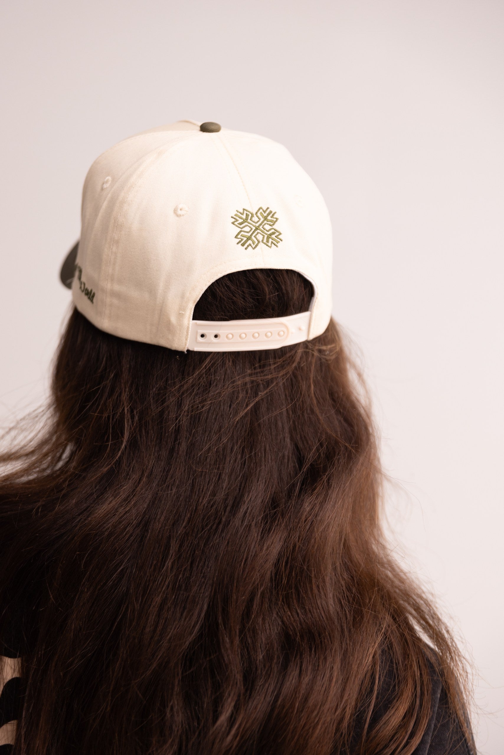 Person wearing a beige cap with a logo on the back against a plain background