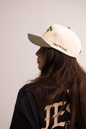 Person wearing a cap with text and a jacket with 'YES' printed on it against a plain background
