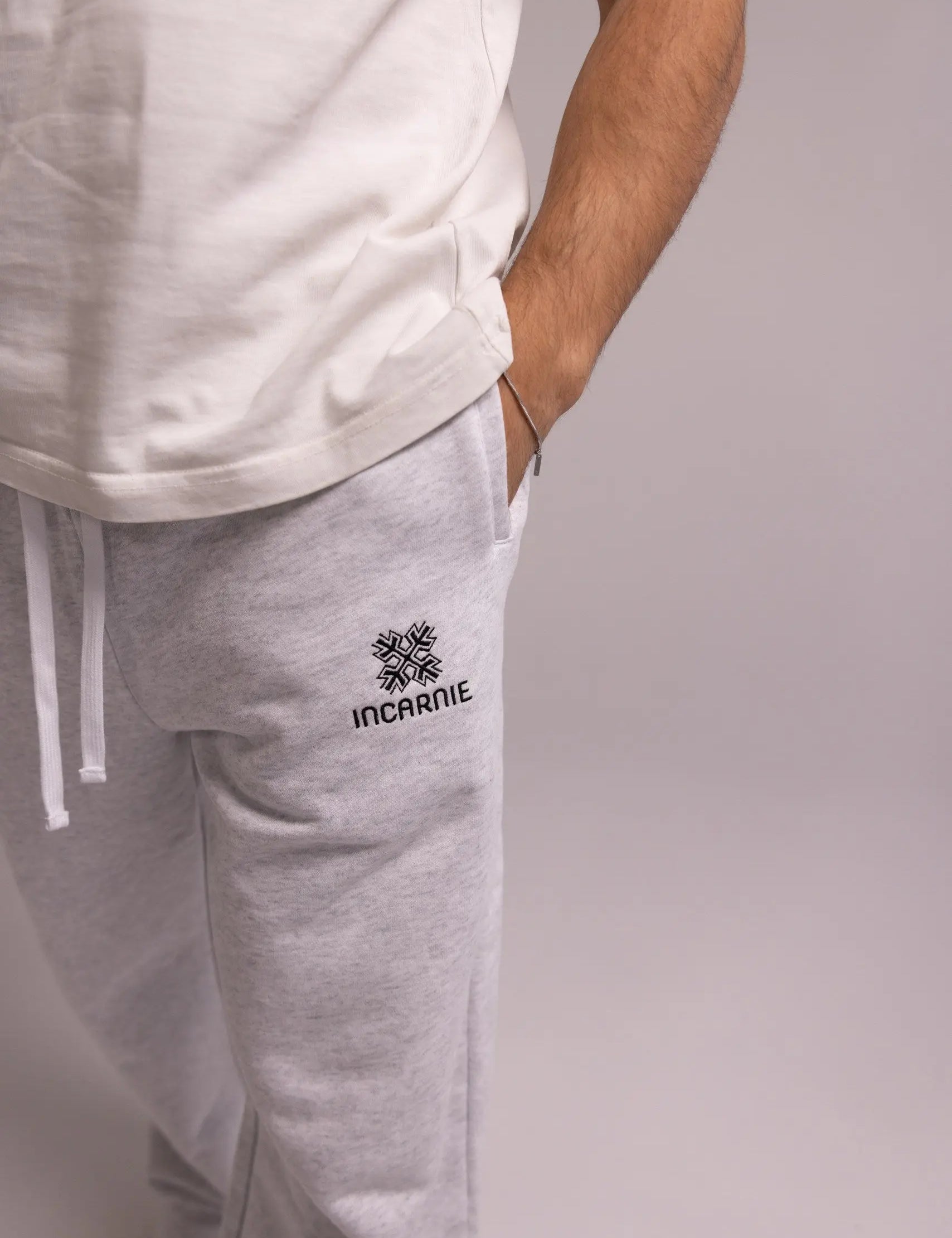 Person wearing gray sweatpants with a brand logo on a plain background