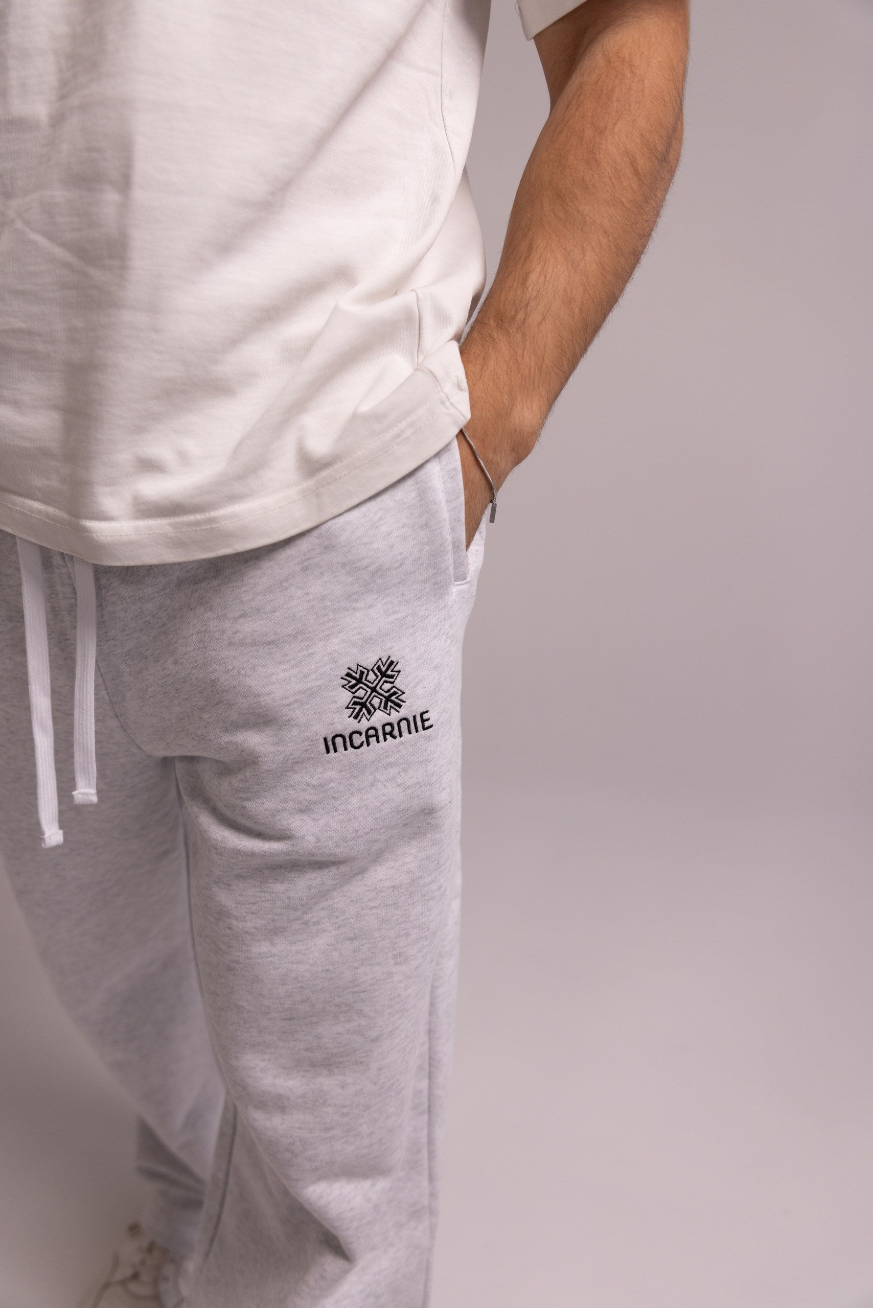 Person wearing gray sweatpants with a brand logo on a plain background