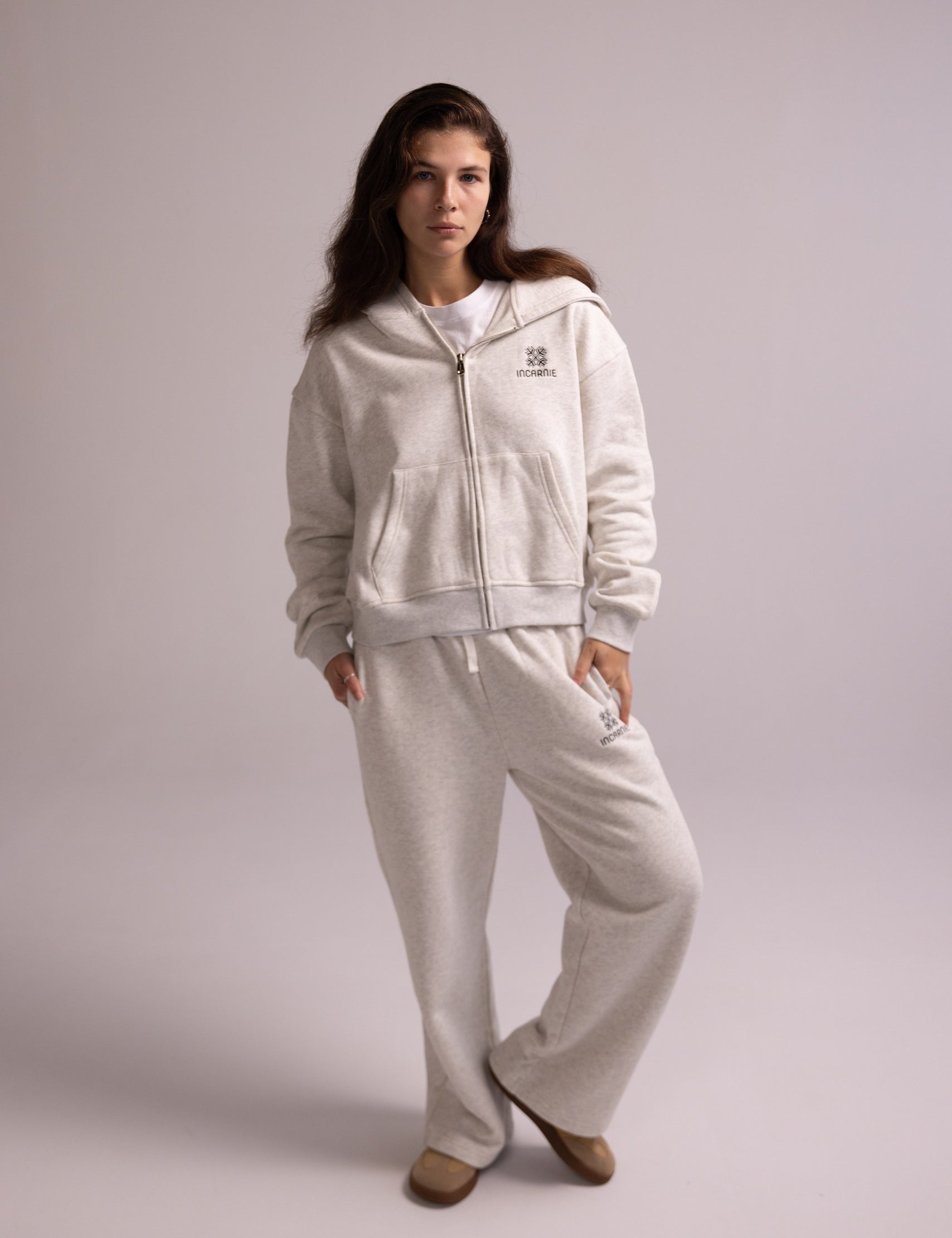 Woman wearing a light gray tracksuit with a logo on a plain background