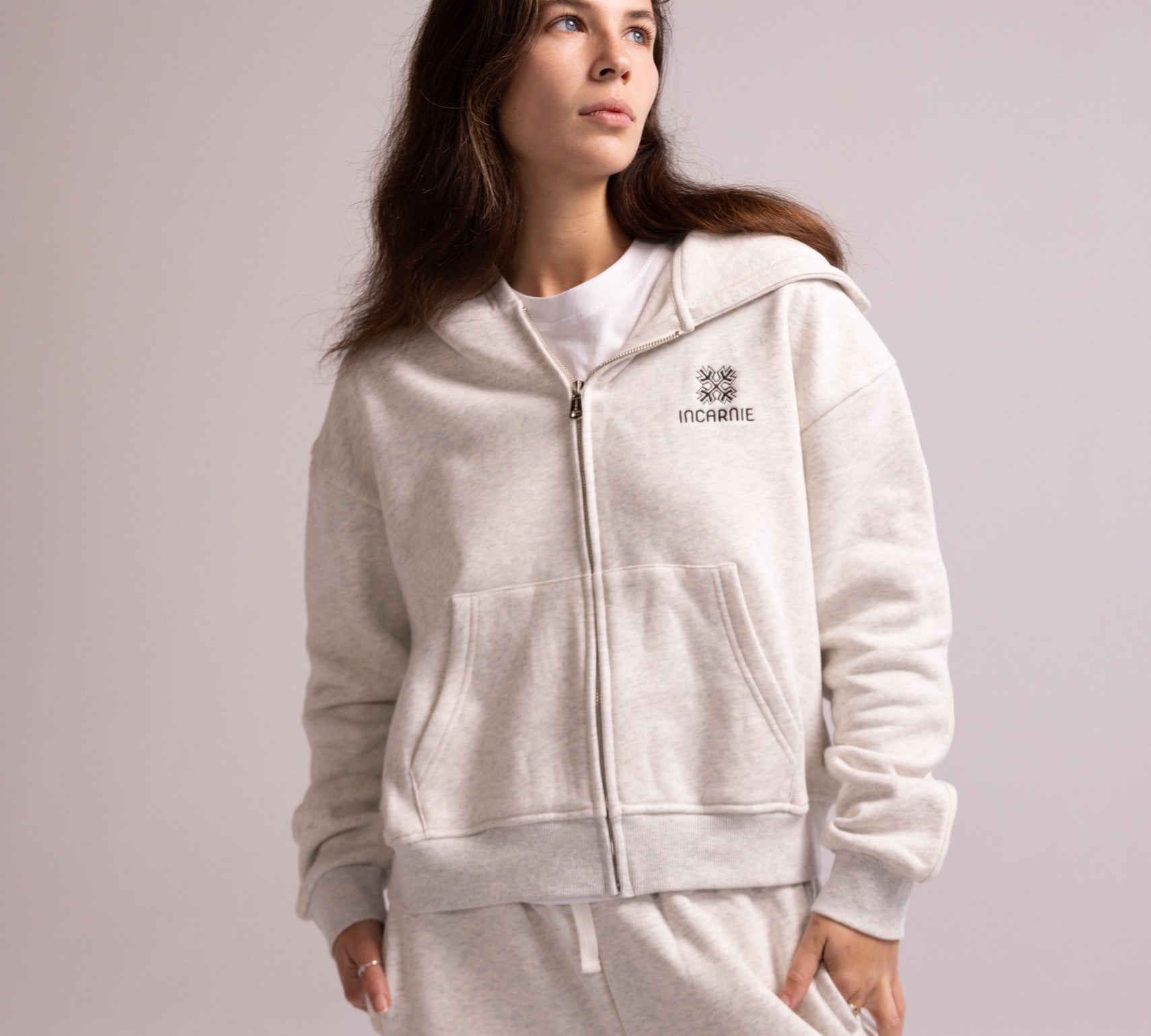 Person wearing a grey tracksuit with a logo on a light gray background