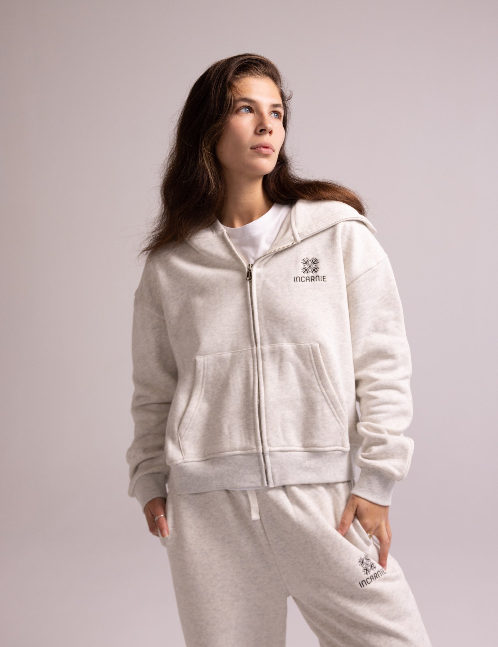 Person wearing a grey tracksuit with a logo on a light gray background