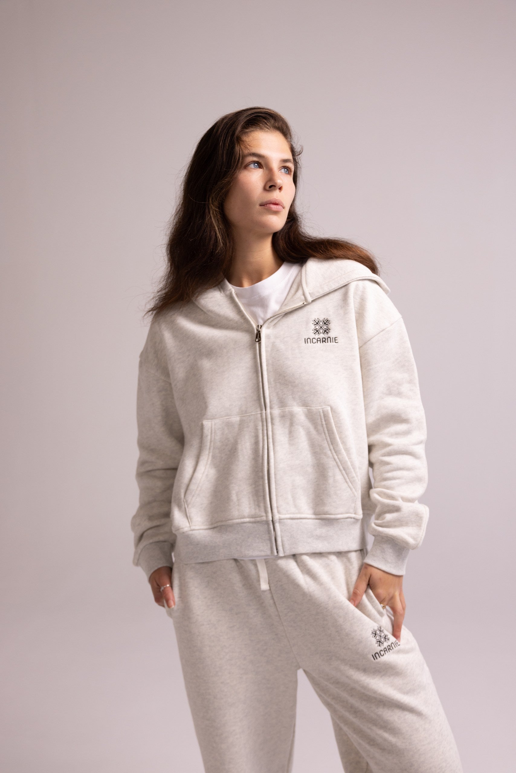 Person wearing a grey tracksuit with a logo on a light gray background