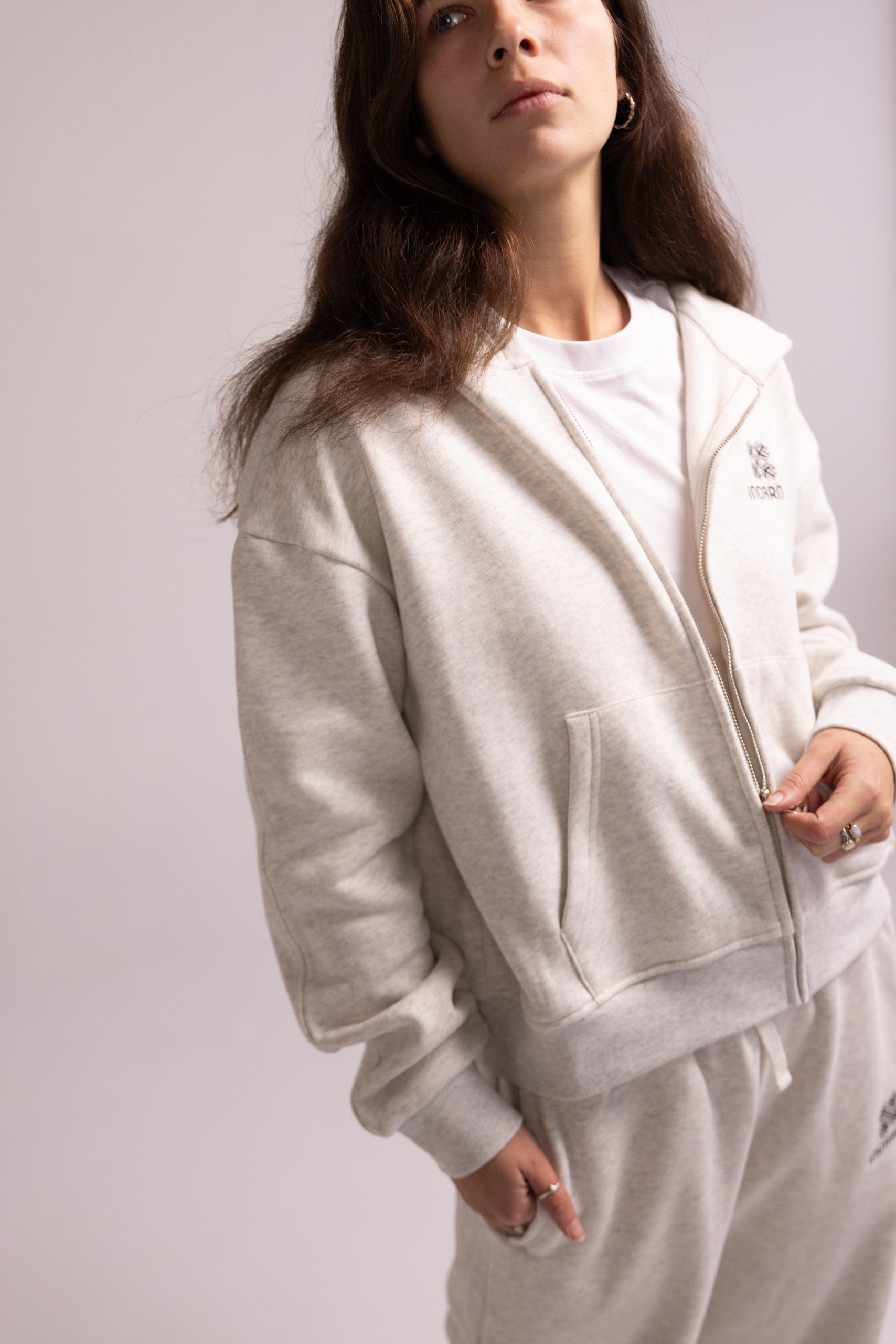 Person wearing a light gray tracksuit with a plain background