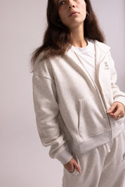 Person wearing a light gray tracksuit with a plain background