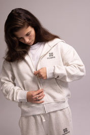 Person wearing a grey hoodie and pants with a brand logo on a gray background