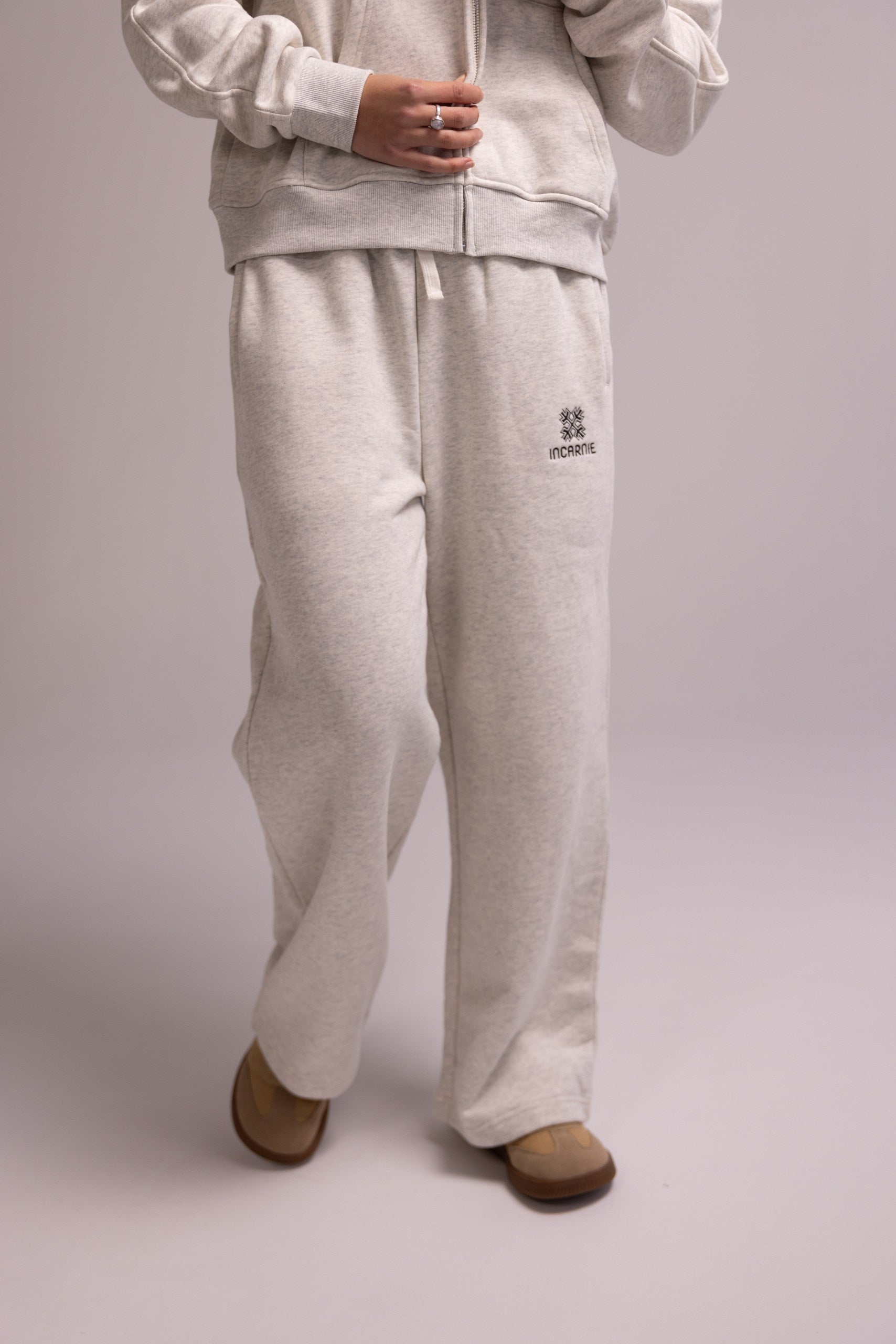 Person wearing a light gray tracksuit with a logo on a plain background