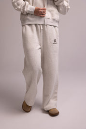Person wearing a light gray tracksuit with a logo on a plain background