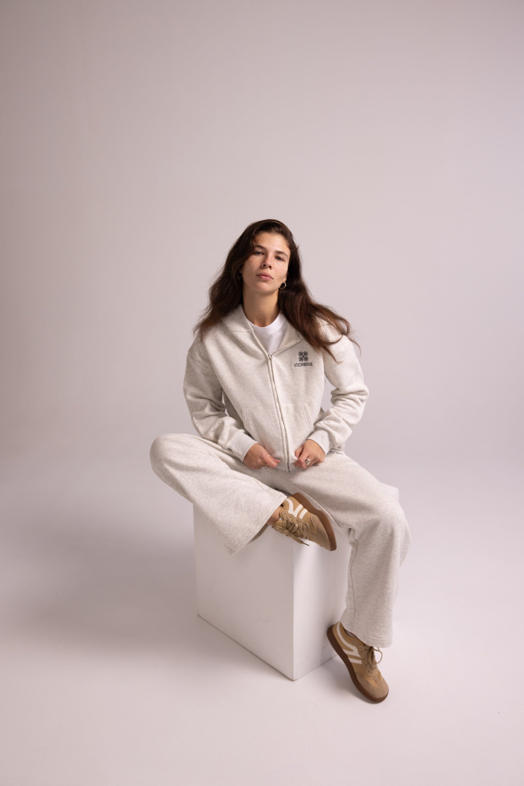 Person wearing a grey tracksuit sitting on a white stool against a plain background