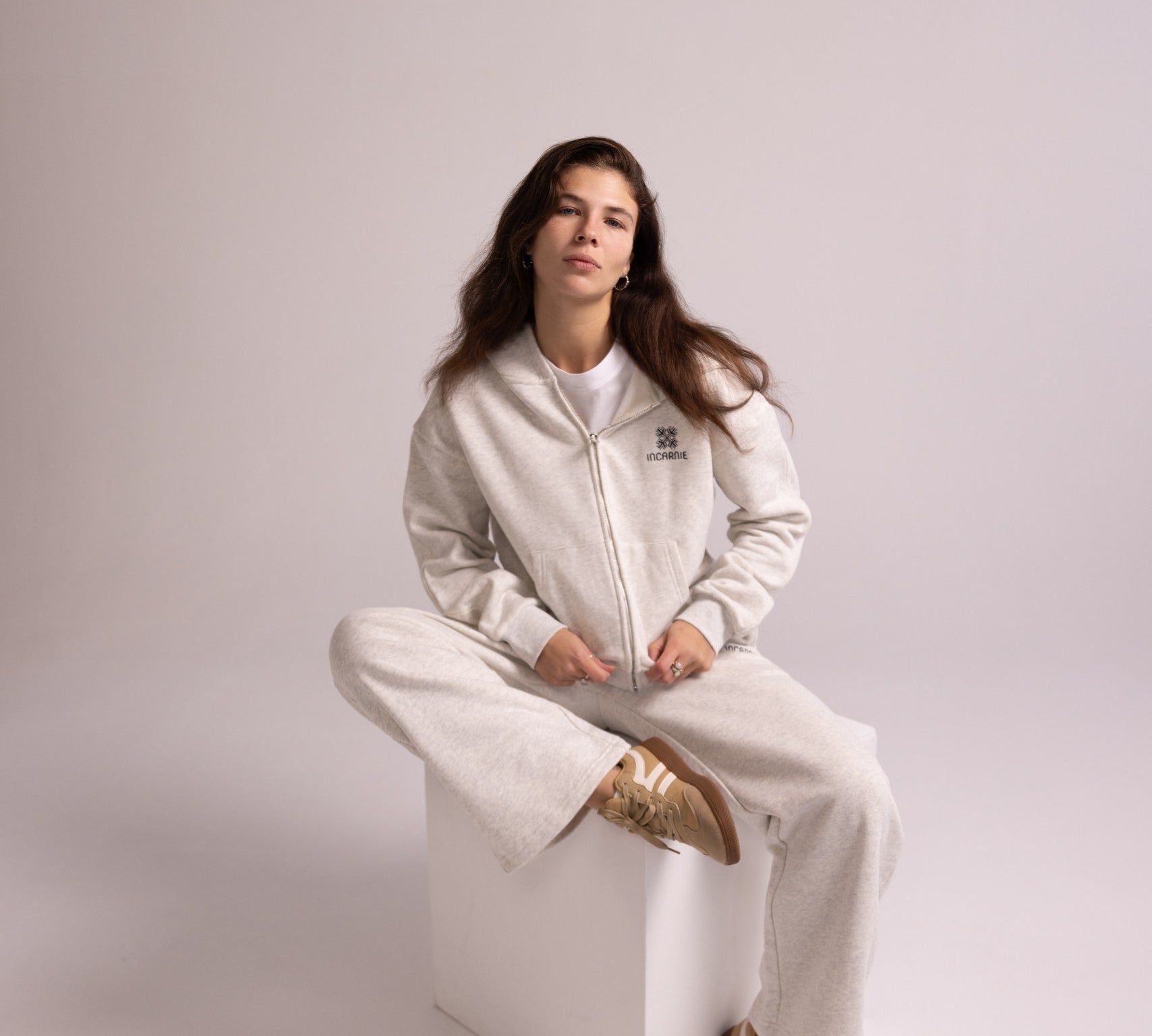 Person wearing a grey tracksuit sitting on a white stool against a plain background