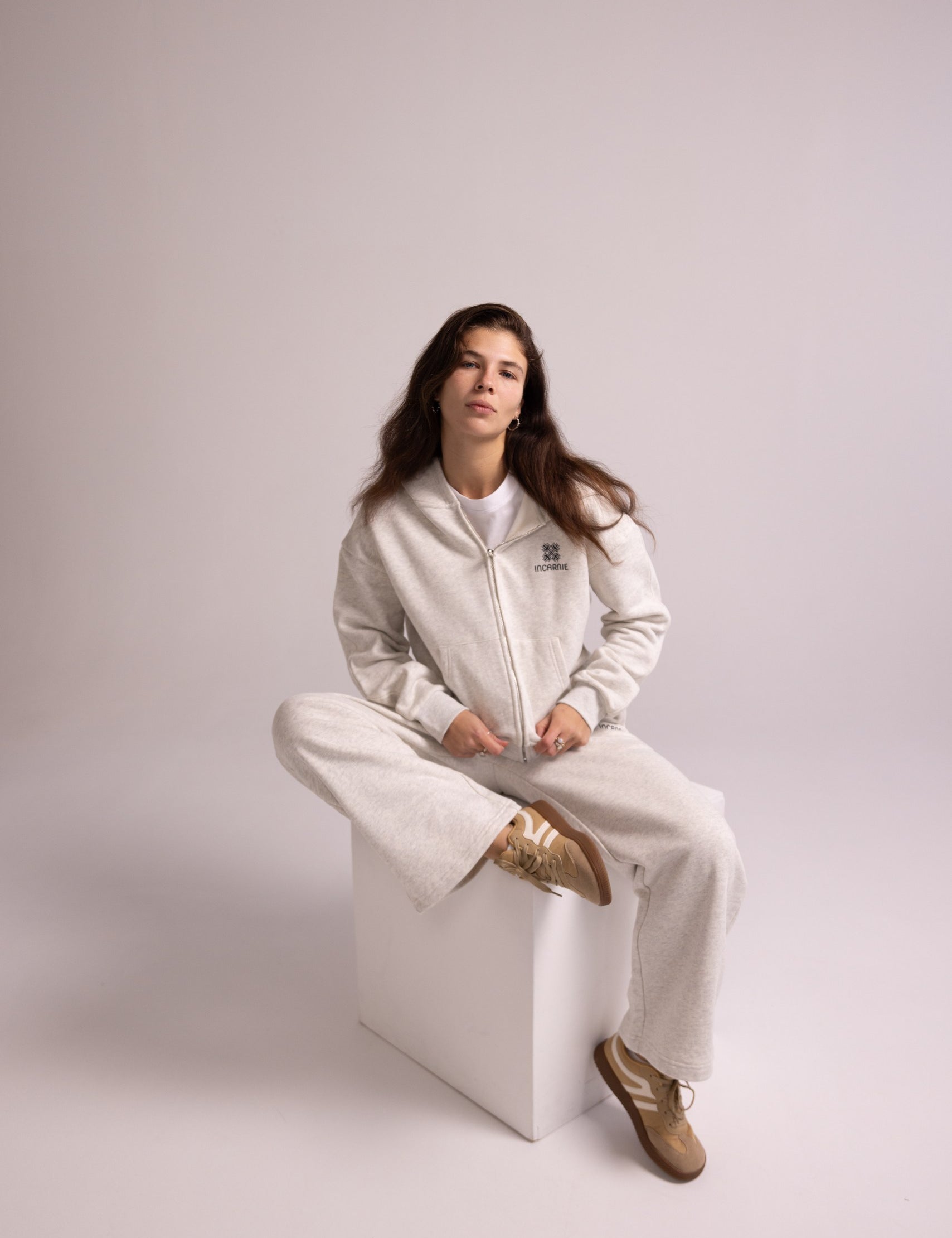 Person wearing a grey tracksuit sitting on a white stool against a plain background