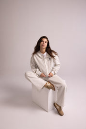 Person wearing a grey tracksuit sitting on a white stool against a plain background