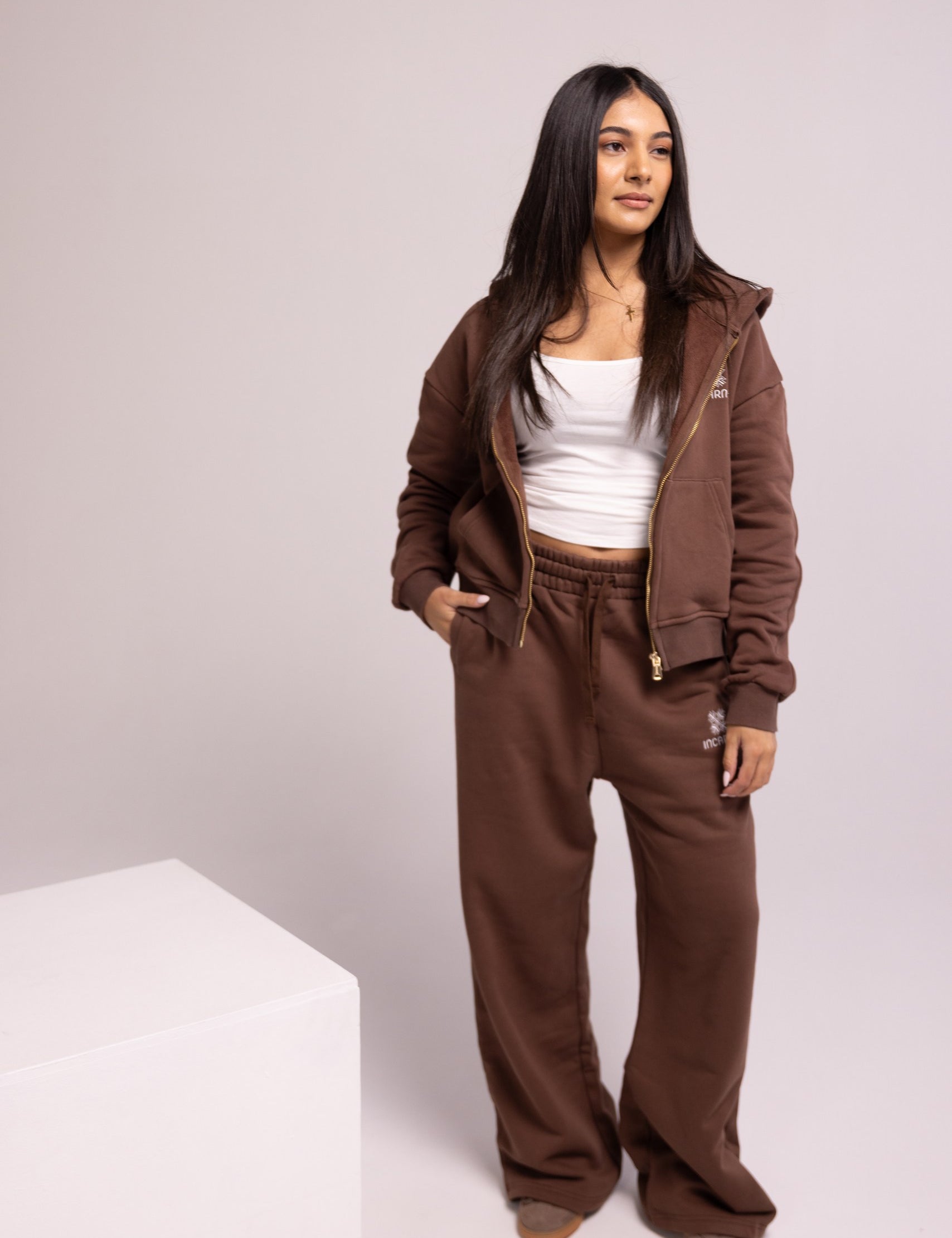 Person wearing a brown tracksuit with a white top on a plain background