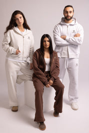 Three people wearing matching tracksuits in white, brown, and gray on a plain background