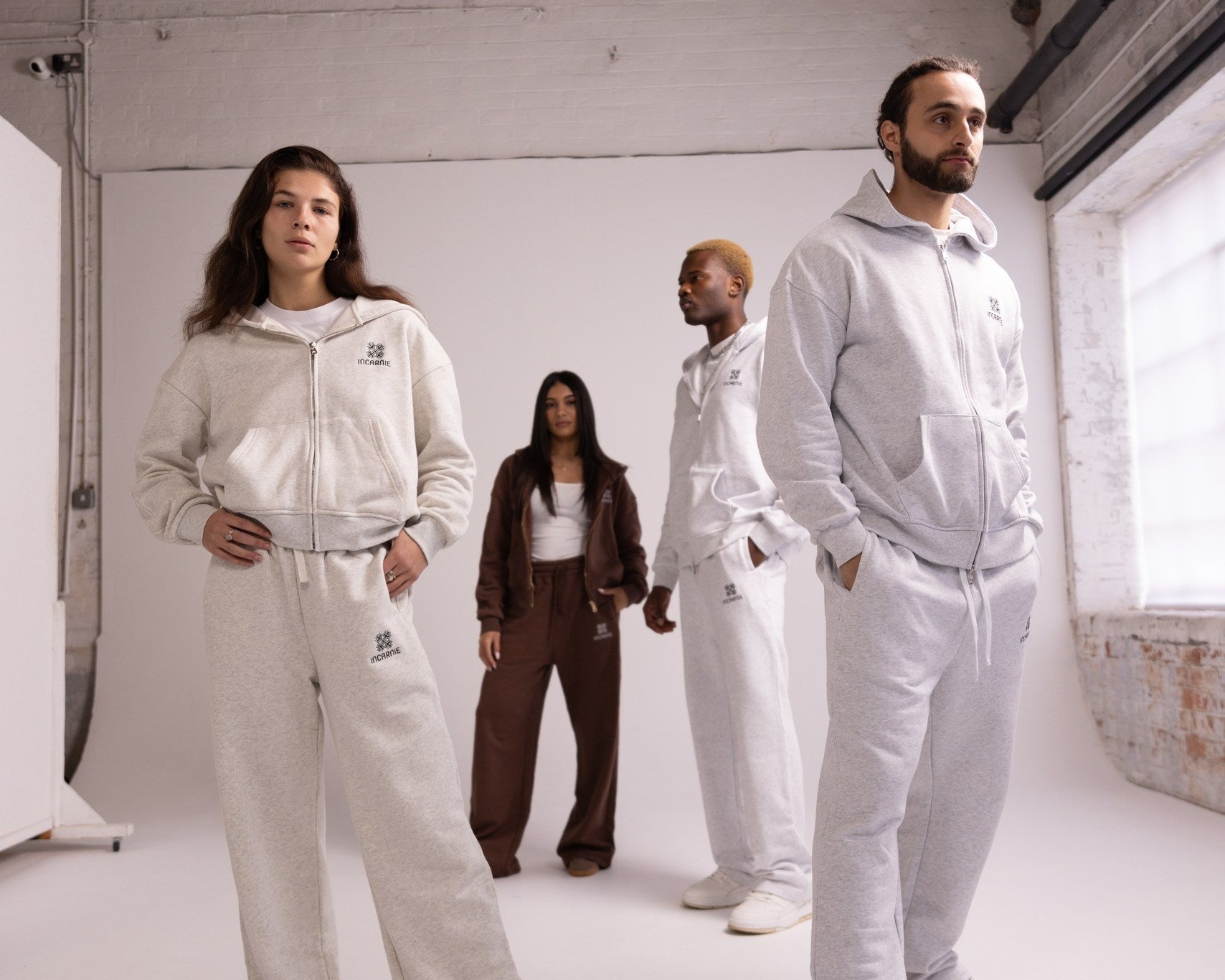Four people wearing matching gray tracksuits in a studio setting.